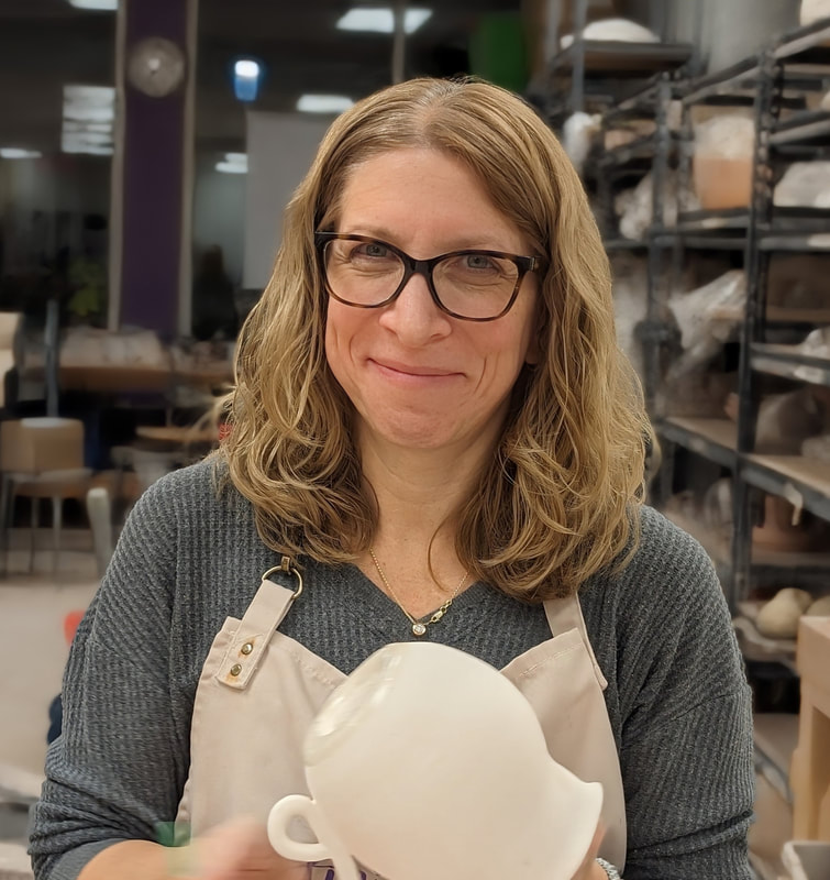 Jill Saxon in a pottery studio holding a white ceramic pot